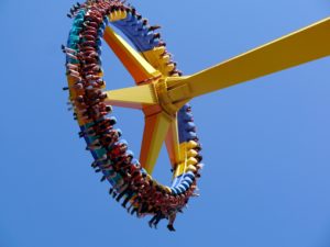 A circular carnival ride high in the air with people's feet dangling off the sides