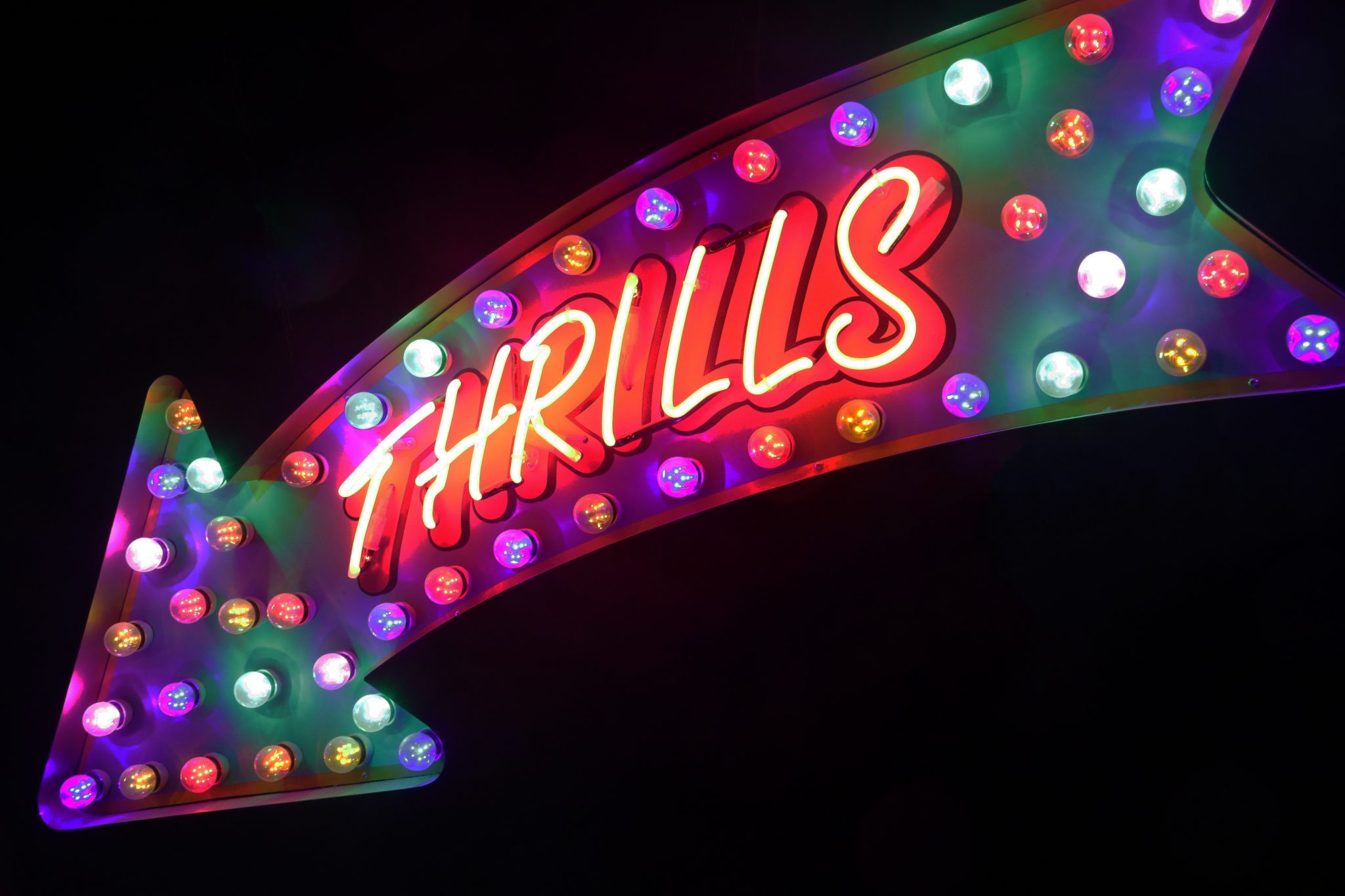 An arrow-shaped neon sign that says "thrills"