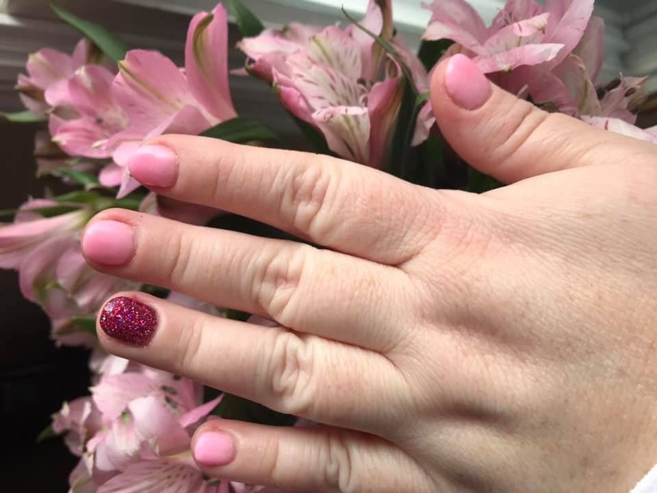 a woman's hand resting on flowers to illustrate dipping your nails with pink polishes