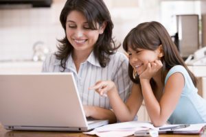 A mom and her daughter smile as they work on a laptop, researching the Enneagram