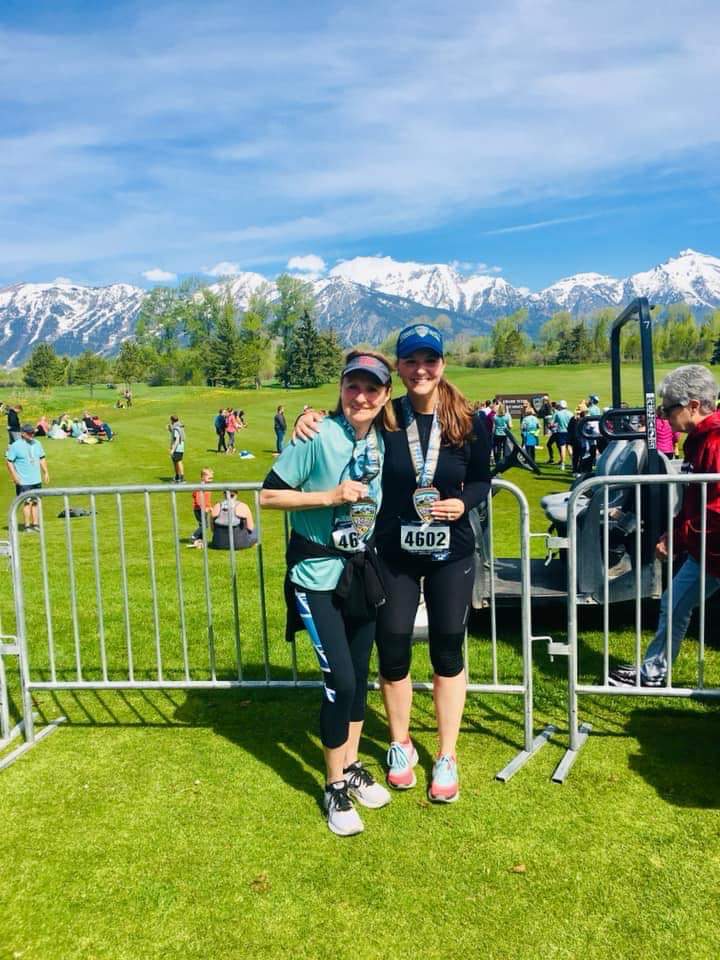 woman and her mom with green grass and mountains behind them after a half-marathon