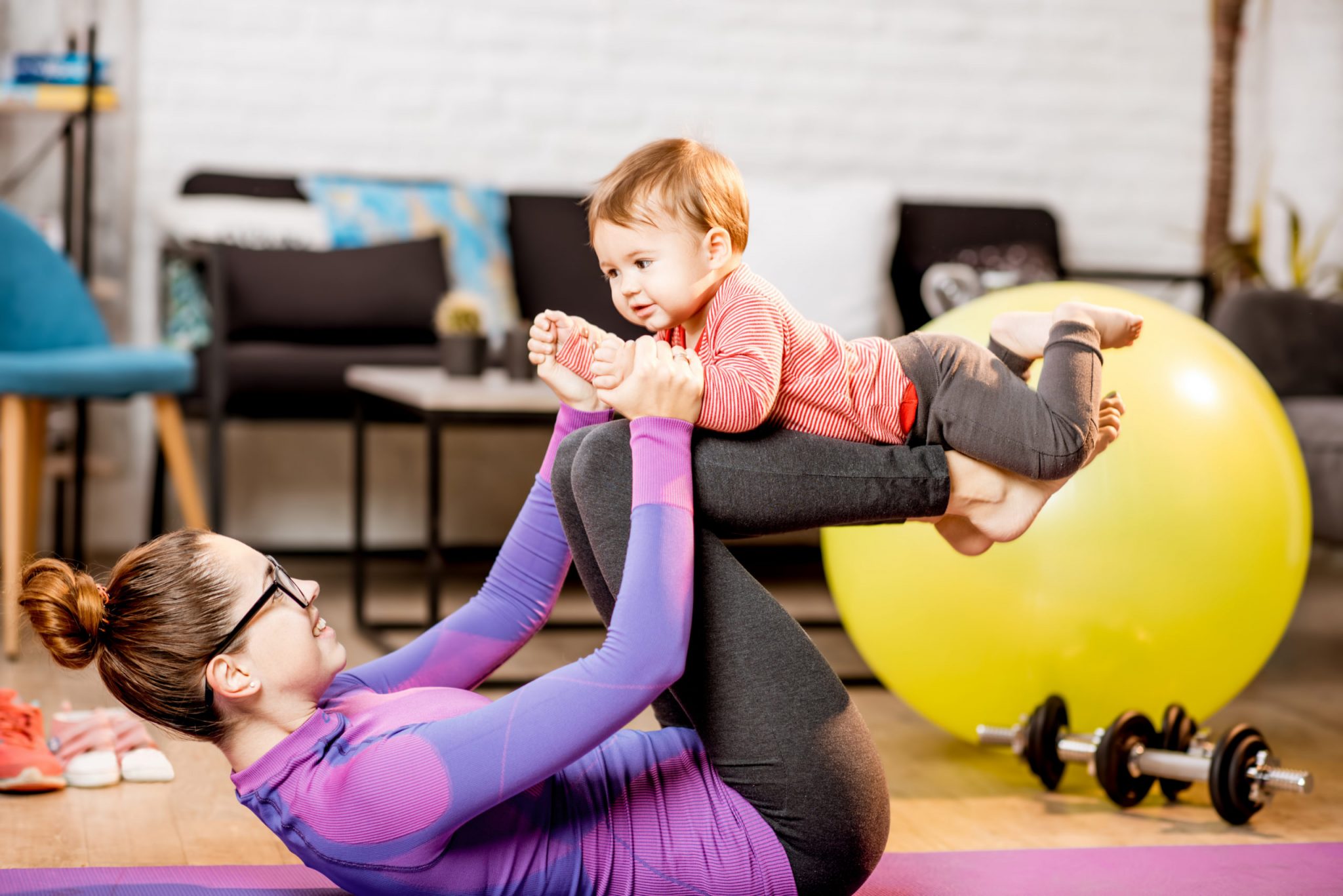 Young mom in sportswear exercising with her child as she bounces him on her knees