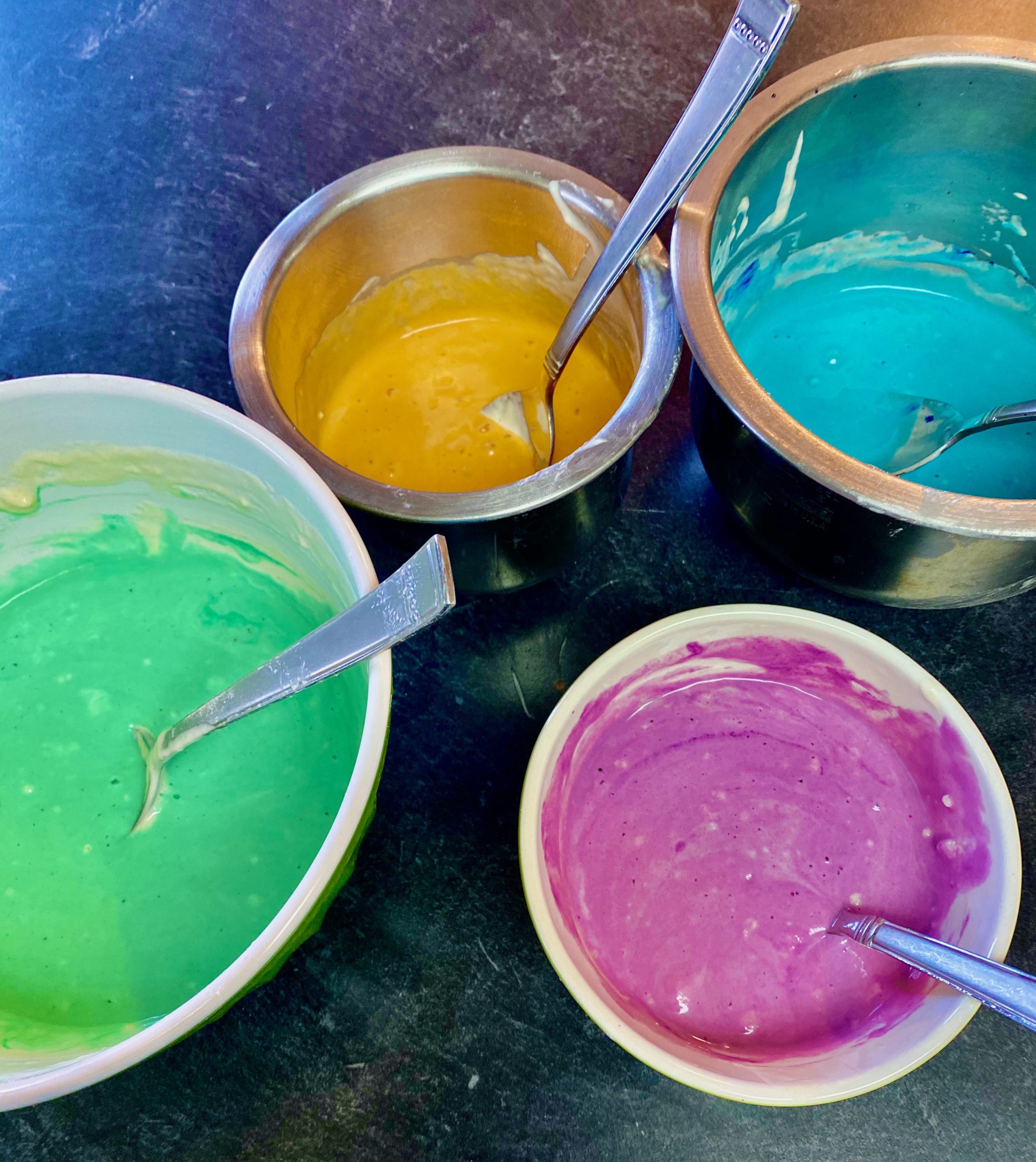 Bowls of pancake batter in four colors: green, orange, blue, and pruple.