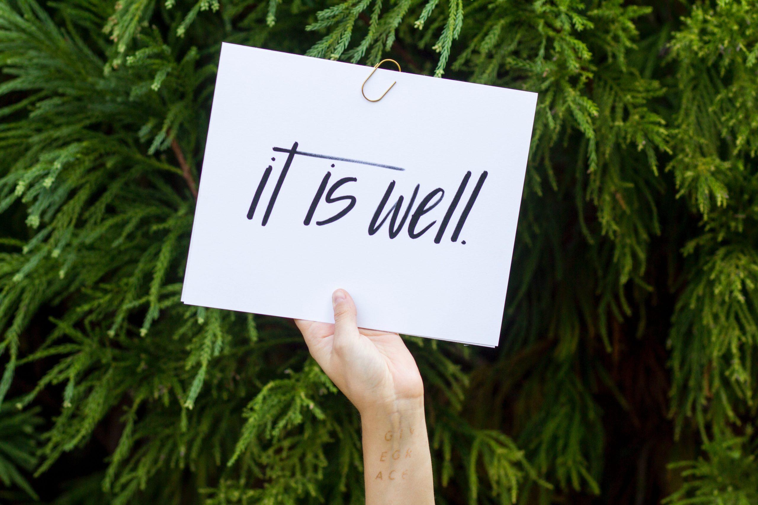 a hand holding up a white sign with black letters saying, "it is well"