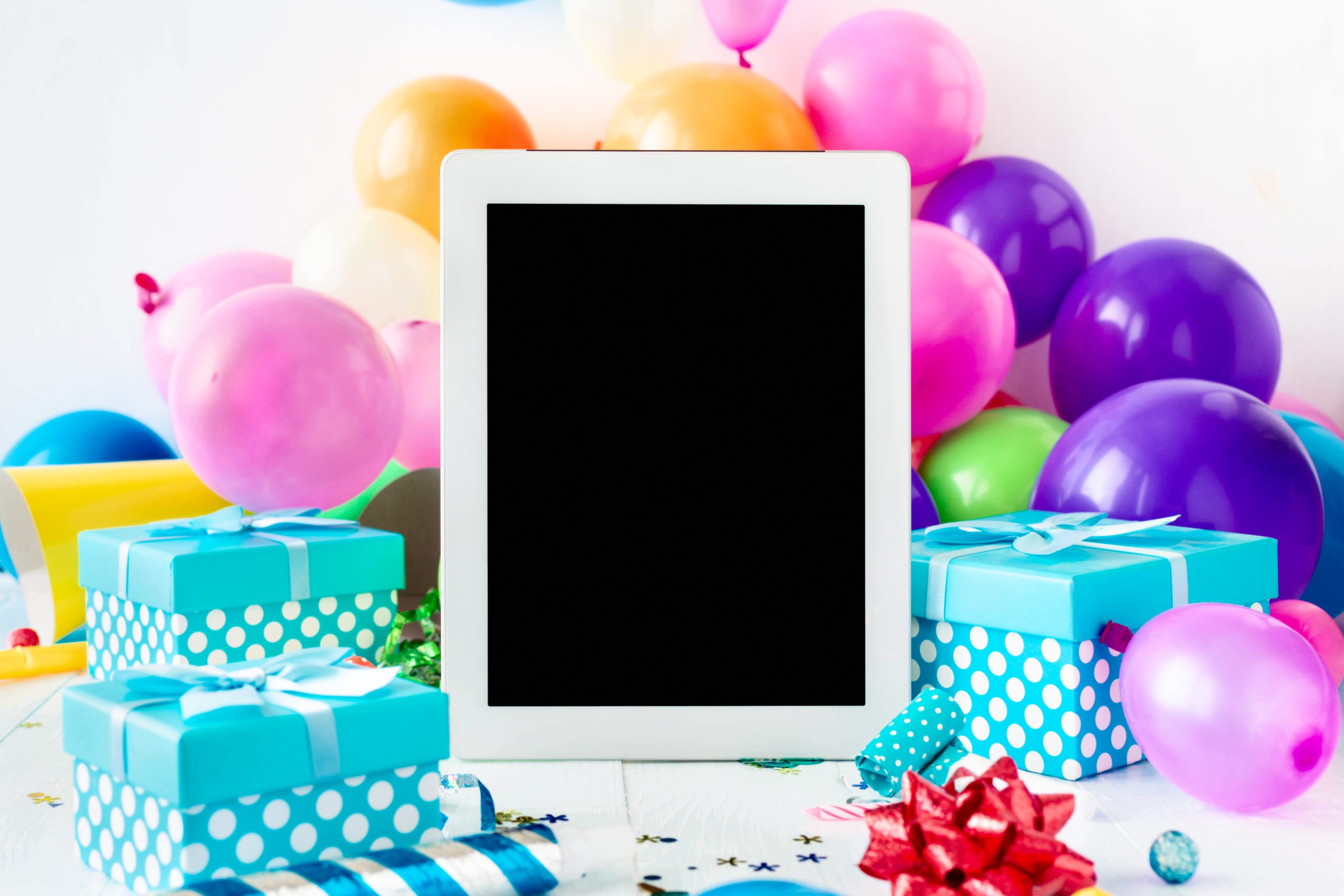 virtual birthday party with a blank tablet screen on a table among balloons and presents