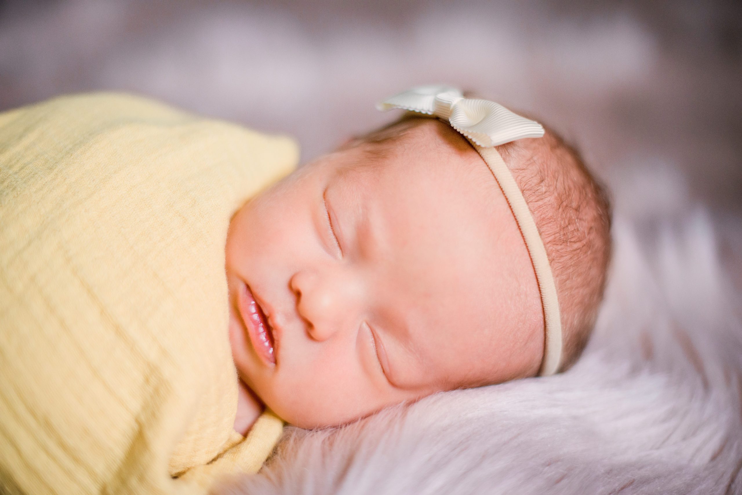 photo of a newborn swaddled in a yellow blanket with a matching yellow bow