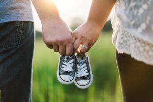 a close up of a man and a woman walking in a field of tall grass as they both hold onto a pair of baby shoes