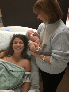 a grandma holding her newborn grandson at the hospital as she stands near her daughter's bed