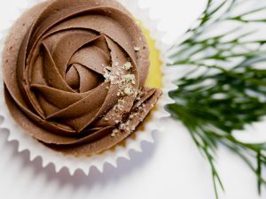 a yellow cupcake with chocolate icing on a white tabletop with sprigs of greenery