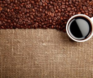 coffee beans on a linen surface with a cup of coffee