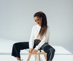 a fashionable African American woman in a white shirt with black pants sitting on a stool