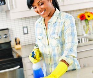 an African American woman wearing yellow rubber gloves as she cleans the kitchen counter