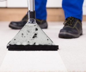 a close up of a man's feet and a carpet cleaning vacuum as he cleans an off white carpet