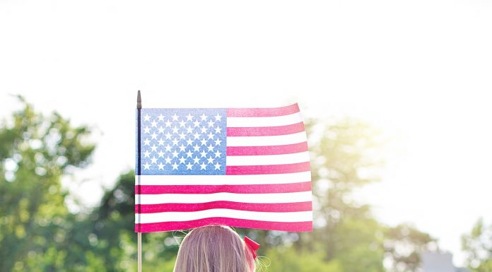 a photo taken of the back of a young girl as she stands in a field, holding the American flag