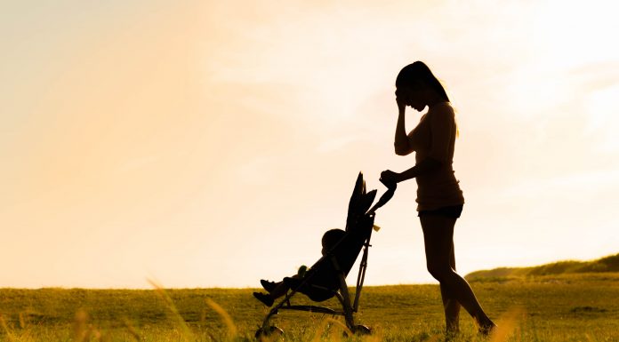 a silhouette of a mom pushing a stroller down a grassy road, with her hand to her forehead in stress
