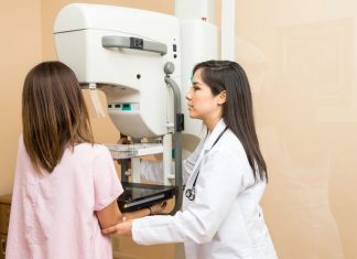 a woman in a pink gown getting help at her mammogram from a doctor in a white lab coat