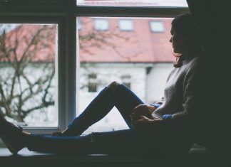 a woman sitting at a window, staring out with a sad look on her face