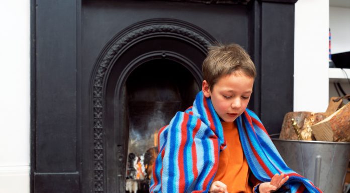 a boy wrapped in a blanket sitting in front of the fireplace with a book