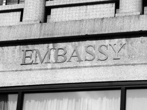 a black and white photo of the word Embassy carved onto a concrete building