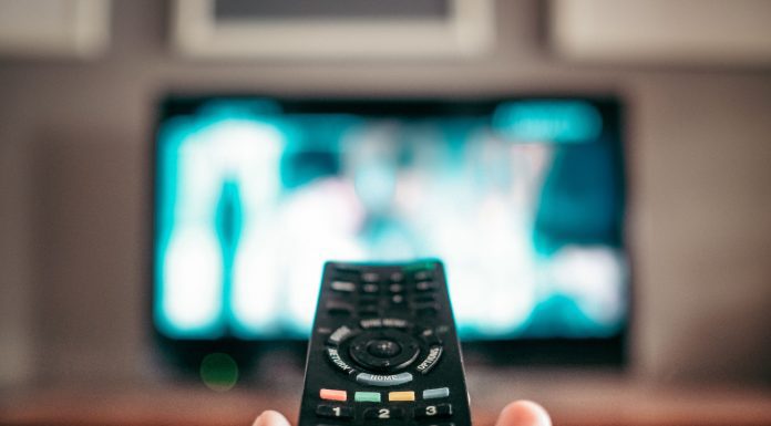 a close up of a hand with a remote, while a TV is blurred in the background