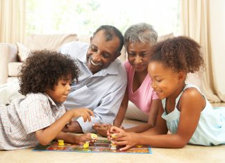 an African American family with grandparents and a young boy and girl laying on the floor playing a board game