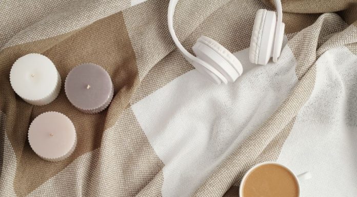 three scented candles, a pair of white headphones, and a cup of coffee on a tan and cream colored blanket