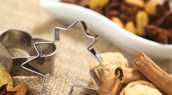 a silver christmas tree cookie cutter with walnuts and cinnamon sticks