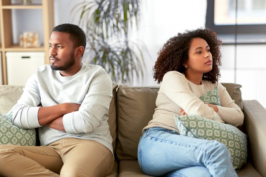 an African American couple, sitting on the couch with arms crossed, looking away from each other as they are managing stress