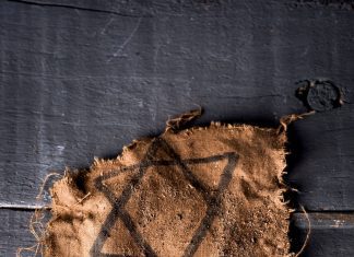 a Jewish star badge and the Hebrew word for "remember" on scraps laying on a wooden table