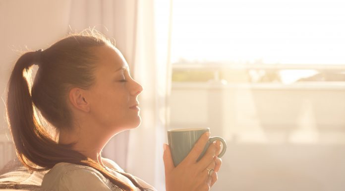 a woman sitting on a couch, eyes closed, inhaling the aroma from a steaming cup of coffee