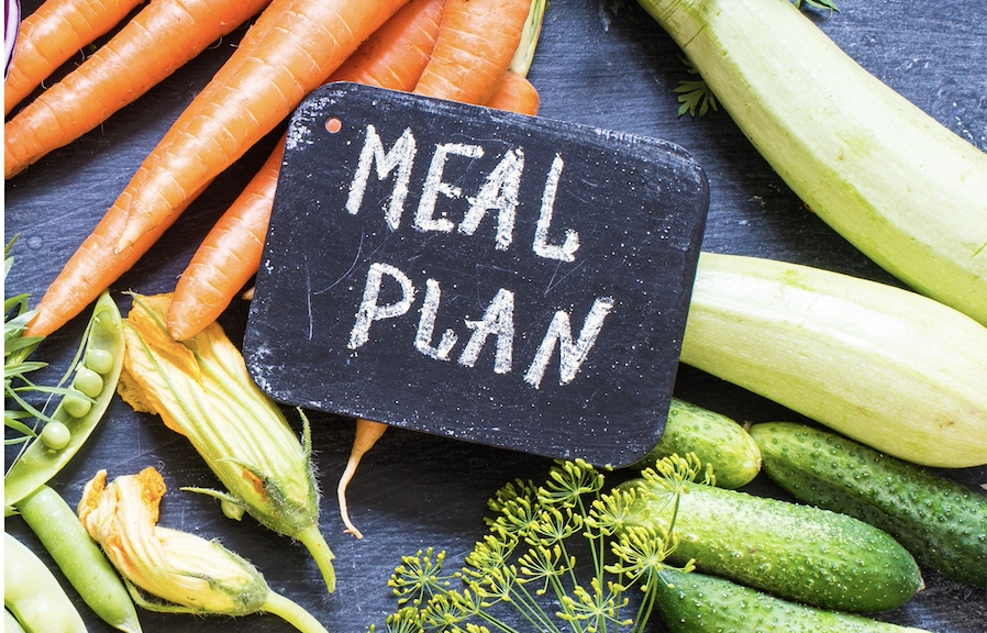 the words "meal plan" written with chalk on a small slate on a counter full of vegetables