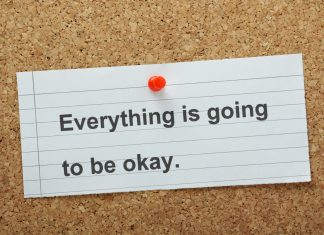 a white notecard that says, "Everything is going to be okay" pinned to a cork board with a red tack.