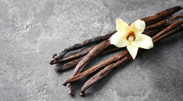 a cluster of vanilla beans with a vanilla flower on top on a marble tabletop