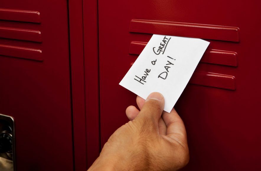 a hand slipping a note into a locker that says, "have a great day"