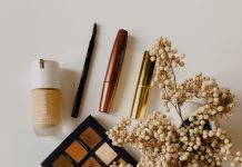 clean skincare and beauty products such as a pallet of brown eyeshadow, mascara, and foundation, on a cream colored background with flowers