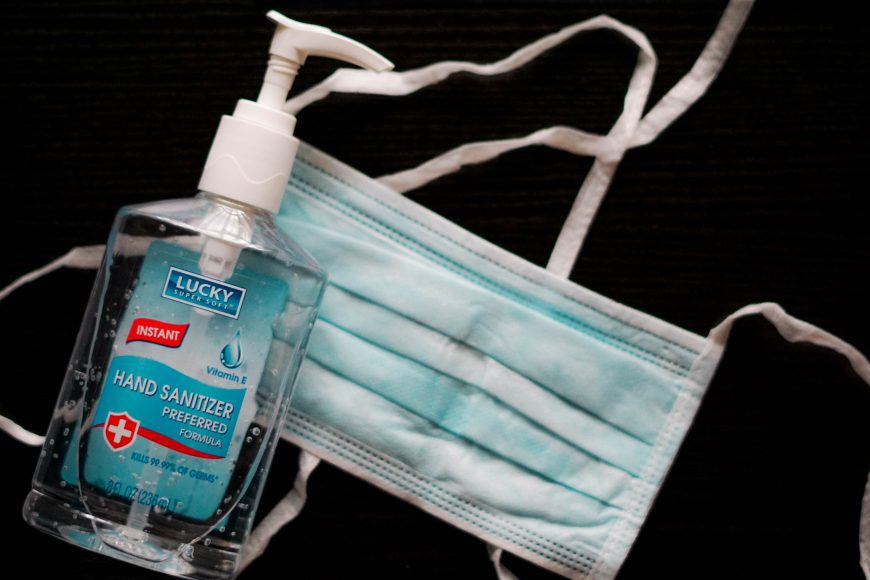 a bottle of hand sanitizer next to a disposable mask on a black background