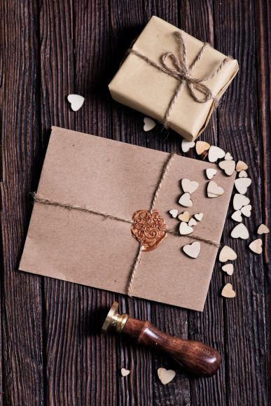 a letter sealed with wax on a table next to a small wrapped box and tiny hearts scattered around 