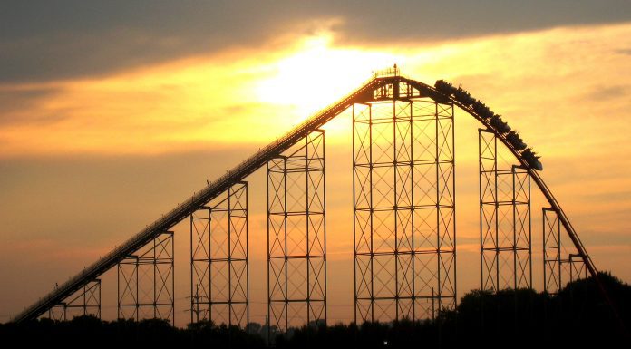 roller coaster cars at the crest of a hill, starting the descent down as the sun sets in the background