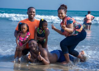 an African American family, posing in the waves on the beach as the mom gives a peace sign