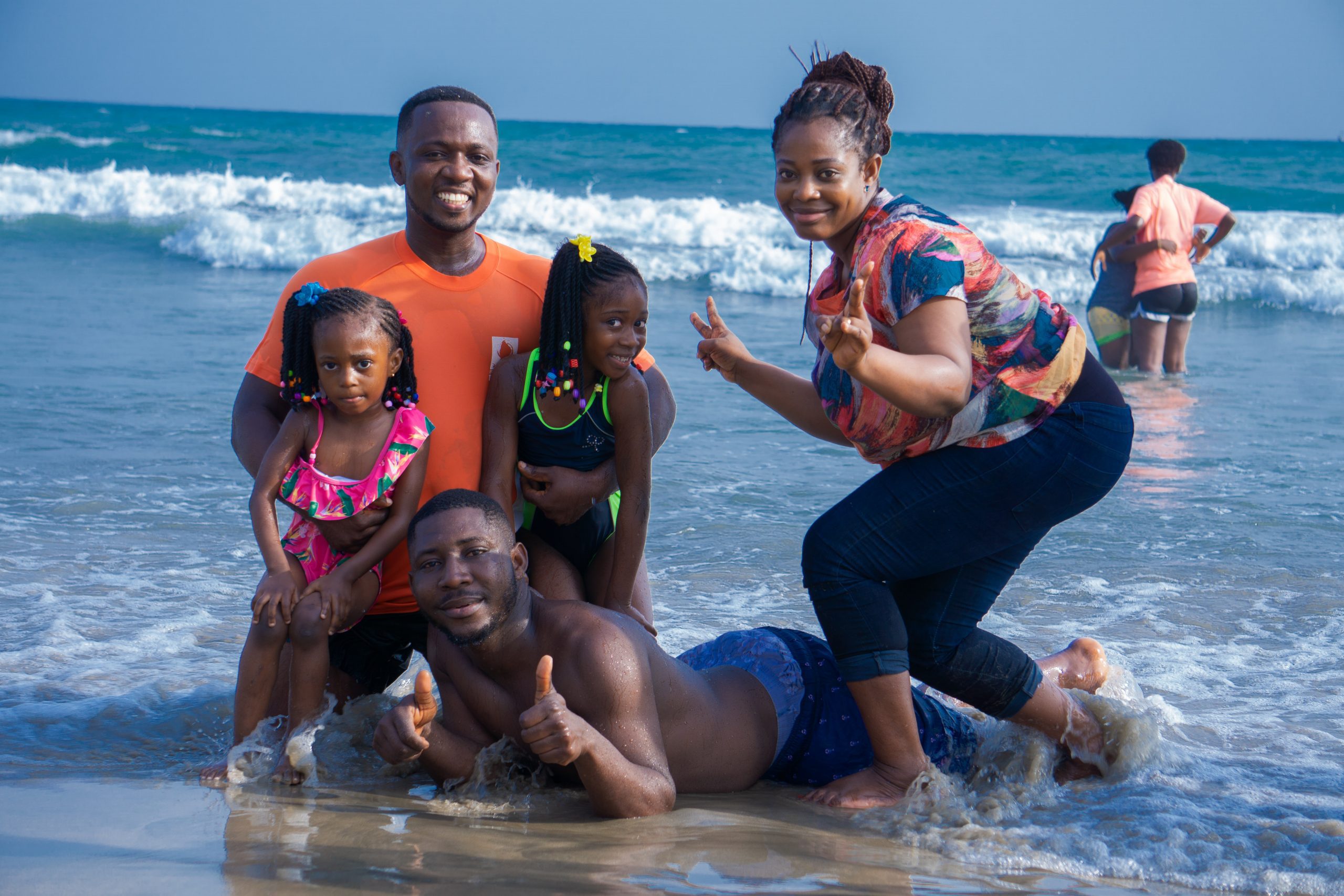 an African American family, posing in the waves on the beach as the mom gives a peace sign 
