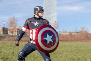 a Captain America Superhero character posing by the St. Louis Arch