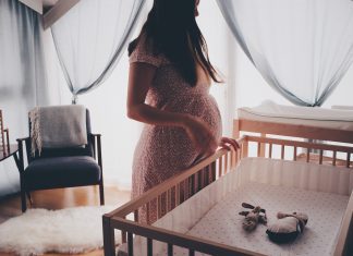 a pregnant mom standing over an empty crib as she prepares for baby in the nesting process