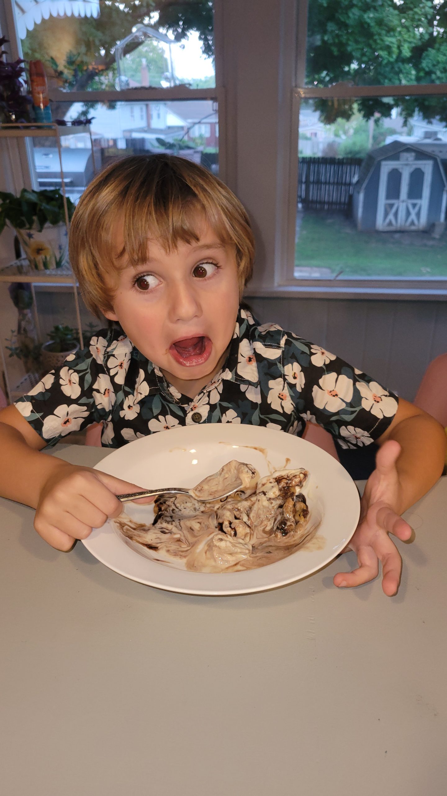 a boy making a silly face as he eats a bowl of ice cream