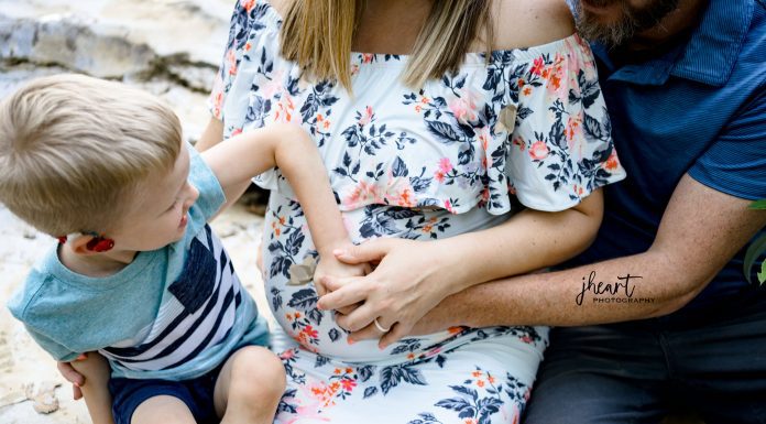 a little boy putting his hand on his mom’s pregnant belly as she gets ready for a C-section