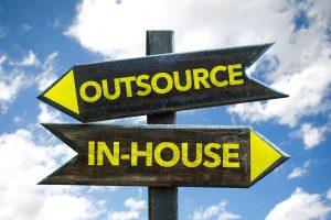 a sign with two arrows- one pointing left with the word “outsource” and one pointing right with the words “in-house” as it applies to business and outsourcing