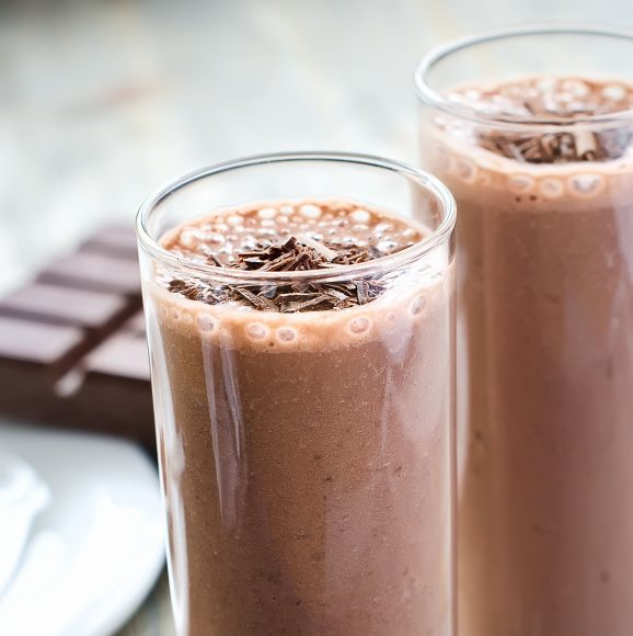two glasses of chocolate smoothie with a chocolate bar in the background
