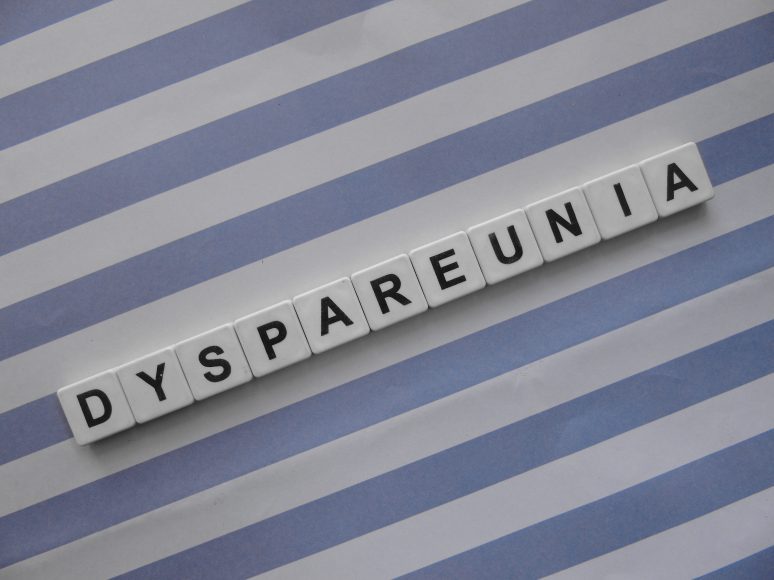letter tiles that spell out the word “dyspareunia” on a lavender and white striped background