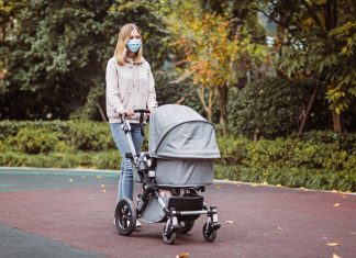 a mom wearing a mask and pushing a baby stroller outdoors