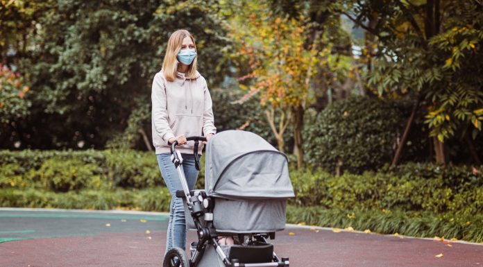 a mom wearing a mask and pushing a baby stroller outdoors