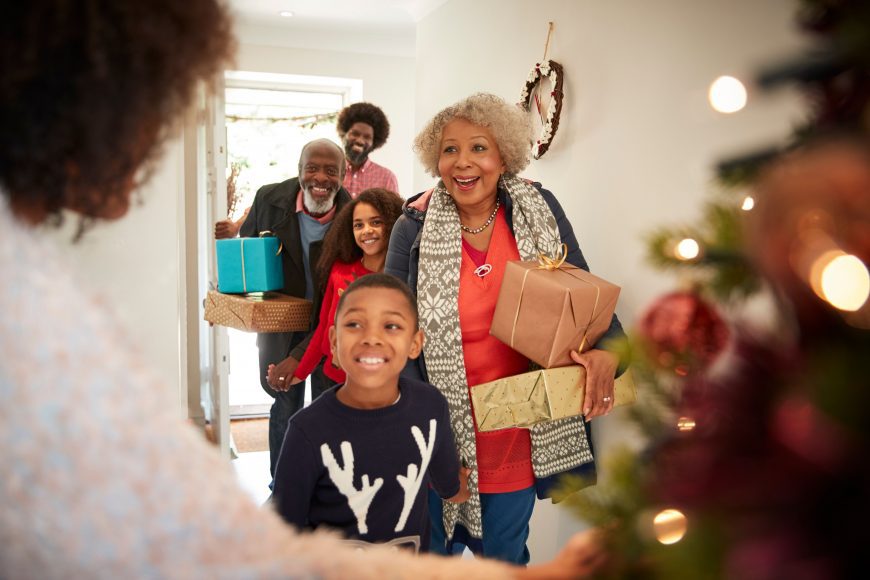 a woman standing near a Christmas tree as she welcomes extended family into her home
